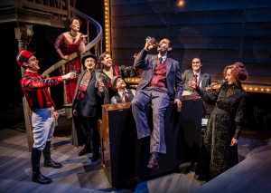Andrew Rothenberg (drinking) and ensemble in Chicago Shakespeare Theater’s production of ROAD SHOW, directed by Gary Griffin.