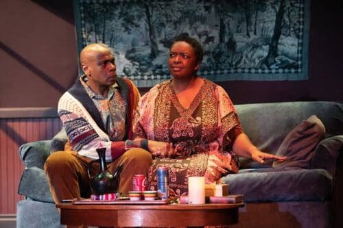 Two people engage in a deep conversation on a couch, surrounded by candles.