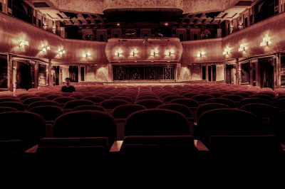 An ornate, empty theater with red velvet seats and a decorated balcony.