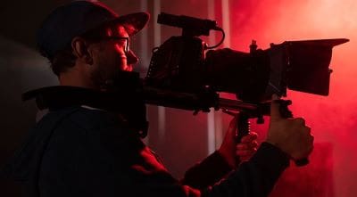 Cameraman filming in a dramatic red-lit environment.