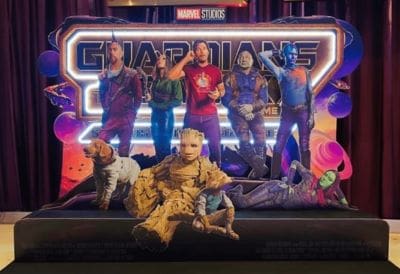 A group of five people and two dogs posing in front of a neon-lit backdrop.