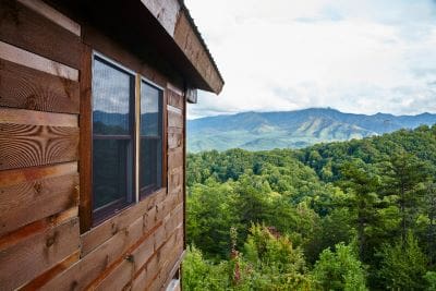 Wooden cabin overlooking lush green forest and distant mountains.
