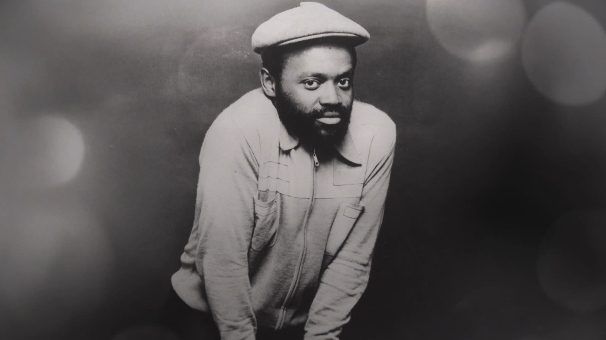 Black and white portrait of a man wearing a cap and casual shirt.