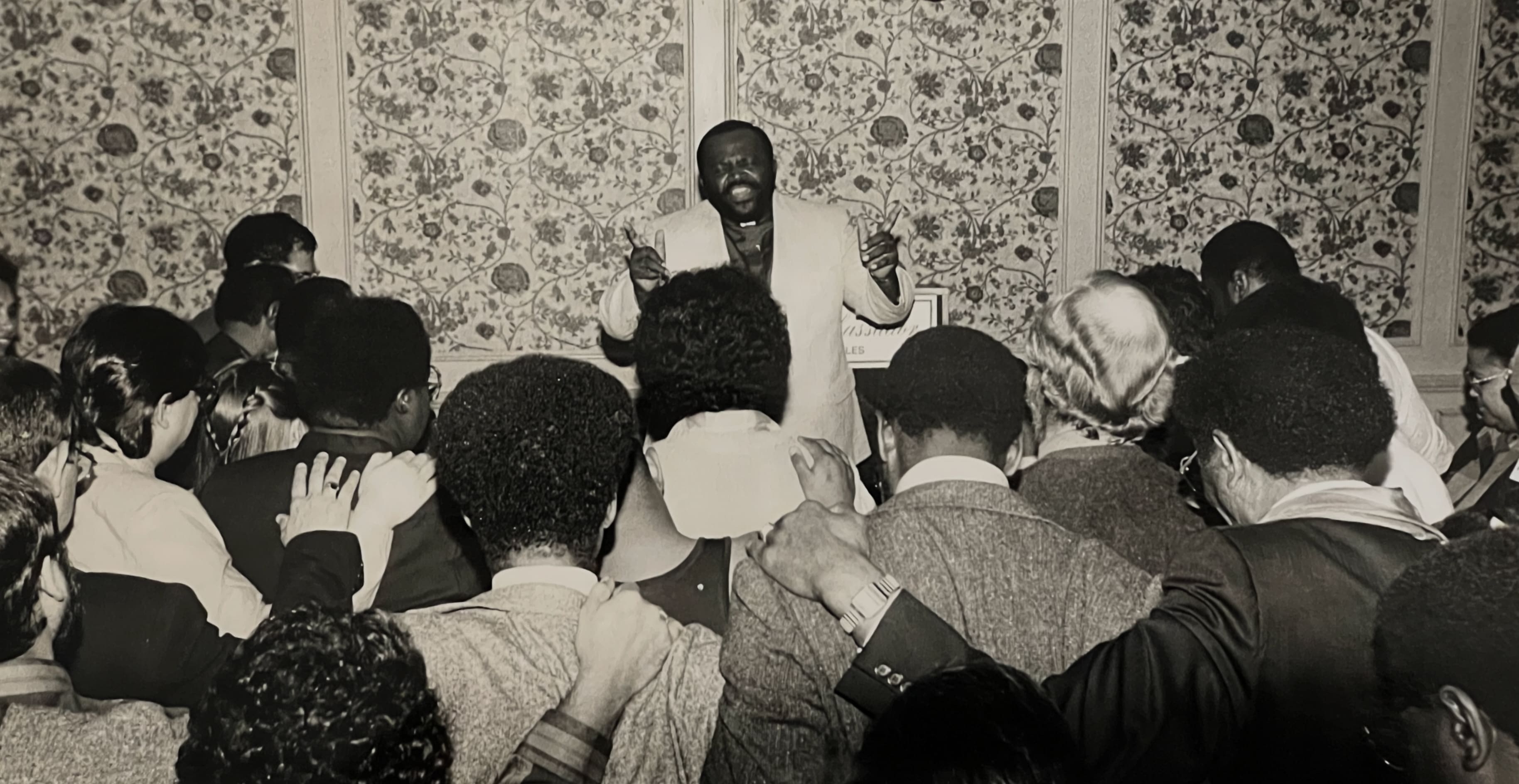 Man speaking passionately to an attentive crowd in a vintage setting.