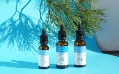Three amber dropper bottles with blue labels on a blue surface against pine branches.