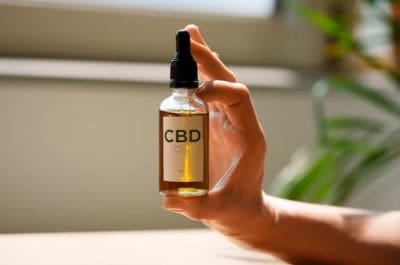 Hand holding a small bottle labeled CBD with a dropper.