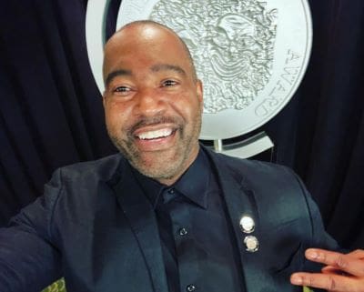 Smiling man in a dark suit taking a selfie.