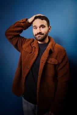 Man in a brown jacket posing against a blue background.