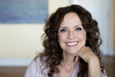 Smiling woman with curly hair resting her chin on her hand.