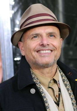 Smiling man in a hat and coat outdoors.