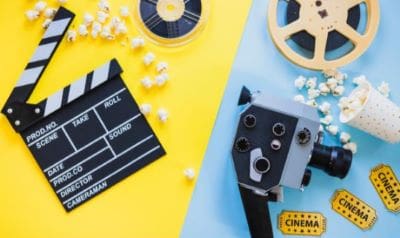 Vintage film camera and movie clapperboard with popcorn on colorful background.