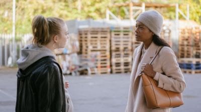 Two women having a conversation outdoors near stacked pallets.