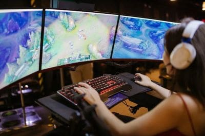Person gaming on a triple-monitor setup with RGB keyboard.