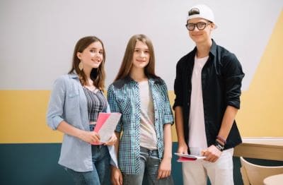 Three young students holding books and smiling.