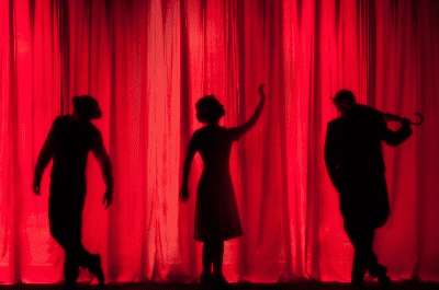 Silhouettes of three people against a vibrant red curtain.