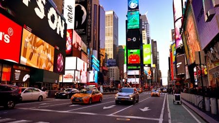 Busy urban street with traffic and illuminated billboards at dusk.