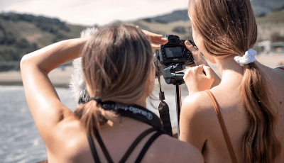 Two women adjusting a camera outdoors during daylight.