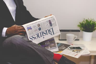 Person reading a business newspaper with coffee nearby.