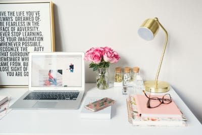 Stylish workspace with laptop, pink flowers, and gold lamp on white desk.