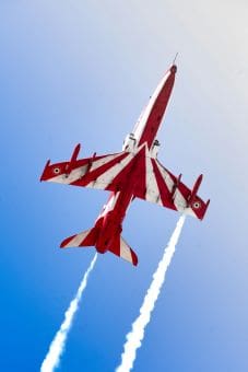 Four red jets flying in tight formation against a clear blue sky.