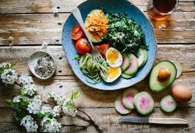 A vibrant bowl of salad with eggs, avocado, tomatoes, and greens on a wooden table.