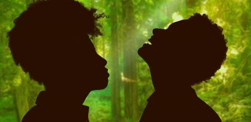 Silhouettes of two people facing each other in a lush green forest.