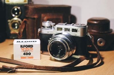 Vintage film camera with Ilford HP5 Plus 400 film box on wooden surface.