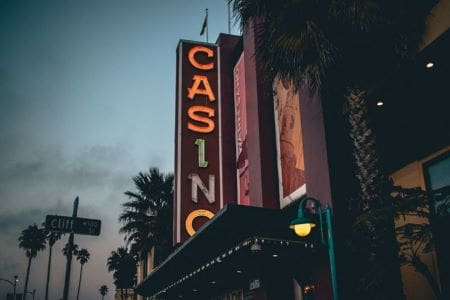 Vintage neon casino sign glowing at dusk on a palm-lined street.