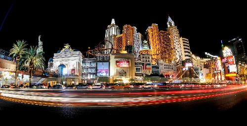 Nighttime cityscape with illuminated skyscrapers and light trails from moving vehicles.