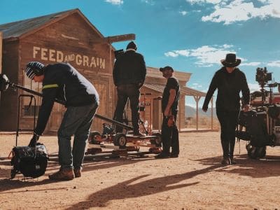 Cowboys working near a vintage train car in a dusty western setting.