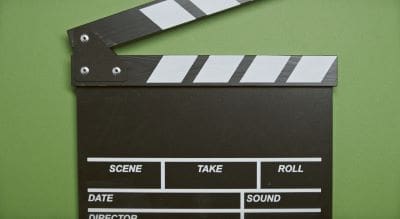A classic black and white film clapperboard on a green background.
