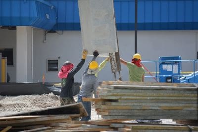 Construction workers lifting a concrete slab at a building site.