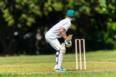 Cricketer in white pads and green helmet prepares to catch a ball.