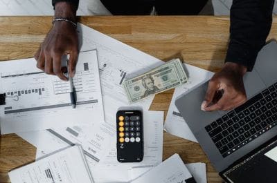 Person managing finances with calculator, cash, and documents on table.
