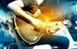 A musician playing an acoustic guitar under warm stage lights.