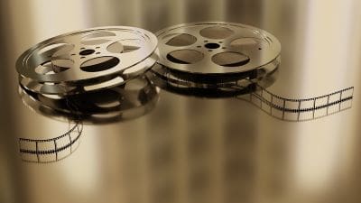 Two vintage film reels with unspooled film on a reflective surface.