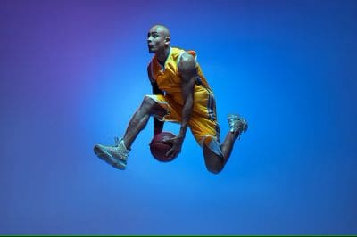 Basketball player in mid-air dunking against a blue background.