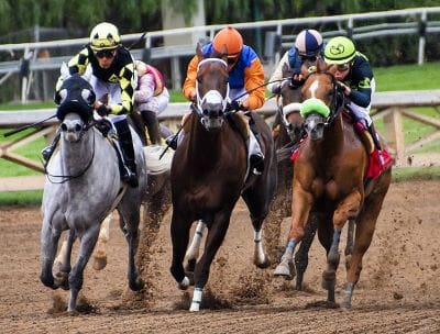 Jockeys racing horses fiercely on a dirt track.