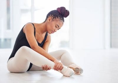 A ballerina adjusting her pointe shoe before dancing.
