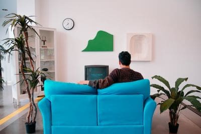 Person sitting on blue couch watching TV in a cozy living room.