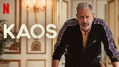 A confident man poses in an elegant room with the word 'KAOS' in bold letters.