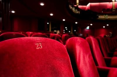 Close-up of plush red theater seats numbered 23 in a dimly lit auditorium.