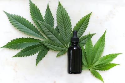 A black dropper bottle on cannabis leaves.