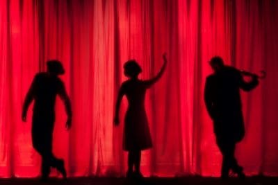 Silhouettes of three people against a vibrant red curtain backdrop.