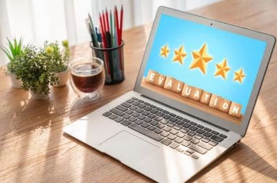 Laptop displaying golden star ratings on a wooden desk with coffee and pencils.
