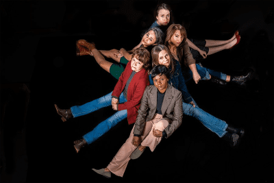Group of six people sitting in a star formation on a black floor.