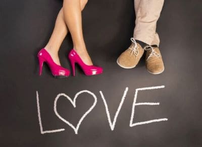 Couple's feet with 'LOVE' written on the ground between them.