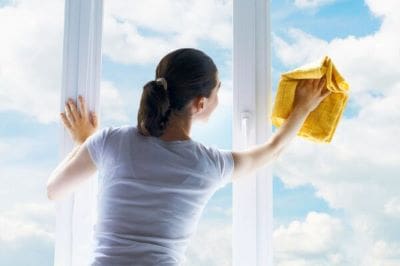 Woman cleaning a large window with a yellow cloth on a sunny day.