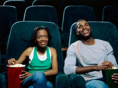 Two women smiling and enjoying a movie in a theater.