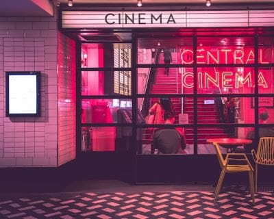 Exterior view of a cinema entrance with neon lighting and a ticket booth.